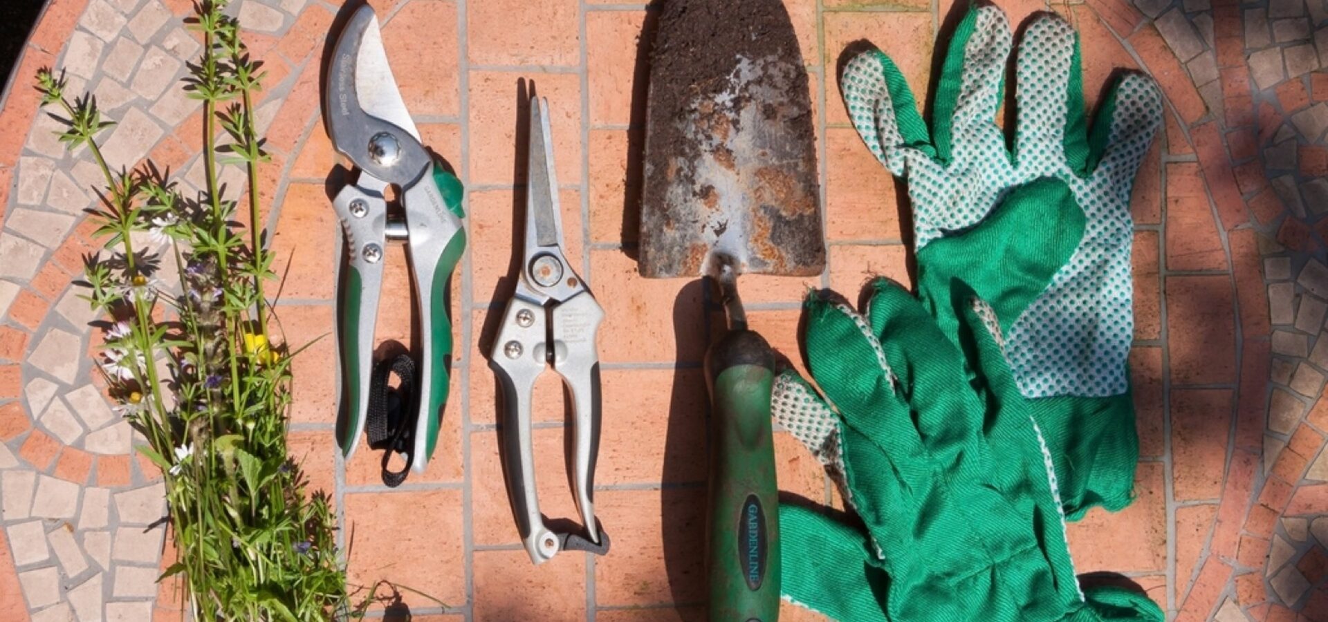 Pruning shears, a trowel and gardening gloves laid out on a tiled patio